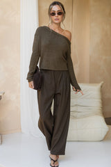 Woman wearing a brown one-shoulder top and wide-leg pants in a minimalistic room.
