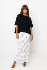 Woman wearing a black top and white patterned skirt on a white background