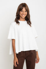 Woman wearing a white blouse and brown pants against a plain background