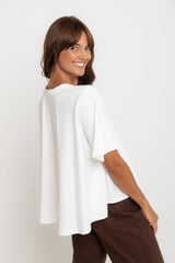 Woman wearing a white top and brown pants on a plain background