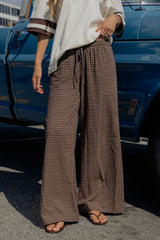 A person wearing brown and beige plaid wide-leg drawstring pants, standing outdoors next to a blue pickup truck.