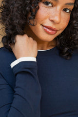 A close-up shot of a woman with curly dark hair wearing a navy blue long-sleeve top with a contrasting white collar trim.