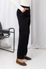 Woman wearing a white long-sleeve top with black tailored trousers, carrying a brown suede bag, on a white background.