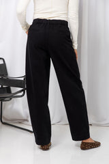 Woman wearing a white long-sleeve top with black tailored trousers, carrying a brown suede bag, on a white background.