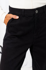 Woman wearing a white long-sleeve top with black tailored trousers, carrying a brown suede bag, on a white background.