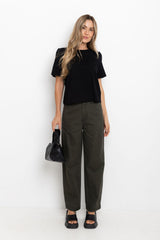 Woman wearing a black top and green pants holding a black handbag on a white background
