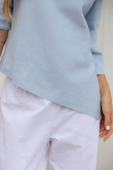 A close-up of a person wearing a light blue ribbed knit top and pale lavender pants, cropped from the shoulders to the upper thighs.