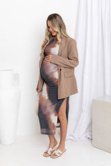 A model with a pregnant belly wearing a sleeveless, fitted mesh midi dress with a watercolour print and a tan blazer over the top.