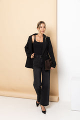 Woman in a black suit standing against a beige wall.