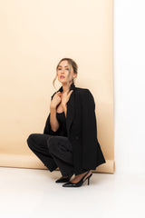 Woman in a black outfit posing against a beige wall
