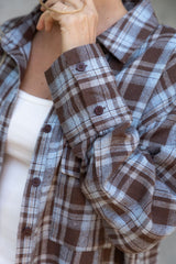 Close-up of a person wearing a brown and blue plaid shirt with a blurred background