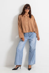 Woman wearing light-wash wide-leg jeans with a sand jacket and black pointed heels, on a white background.