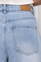 Close-up of the back waistband and pocket of light-wash blue denim jeans, with a small tan leather patch visible at the back waist.