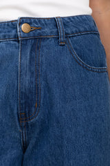Close-up of a person wearing medium blue denim jeans with a visible front pocket, belt loop, and brass-toned button, paired with a white top.