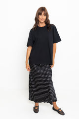 Woman wearing a black oversized t-shirt and a long black and white polka dot skirt on a white background