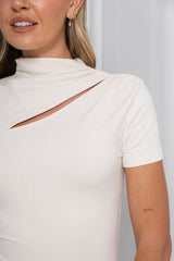 Close-up of a woman wearing a fitted short-sleeve top in a warm off-white or cream color, featuring a mock neck and a diagonal cutout detail across the chest.