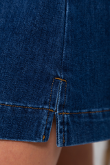 Close-up of dark blue denim shorts showing a split hem with contrast orange stitching and a small portion of the wearer's skin visible.