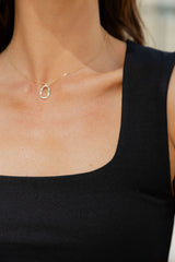A close-up of a model wearing a delicate gold chain necklace with a small, open oval pendant, paired with a black ribbed tank top.