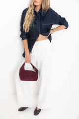 Woman wearing Willow white straight-leg linen pants styled with a dark denim shacket, burgundy suede bag, and burgundy ballet flats