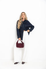 Woman wearing Willow white straight-leg linen pants styled with a dark denim shacket, burgundy suede bag, and burgundy ballet flats