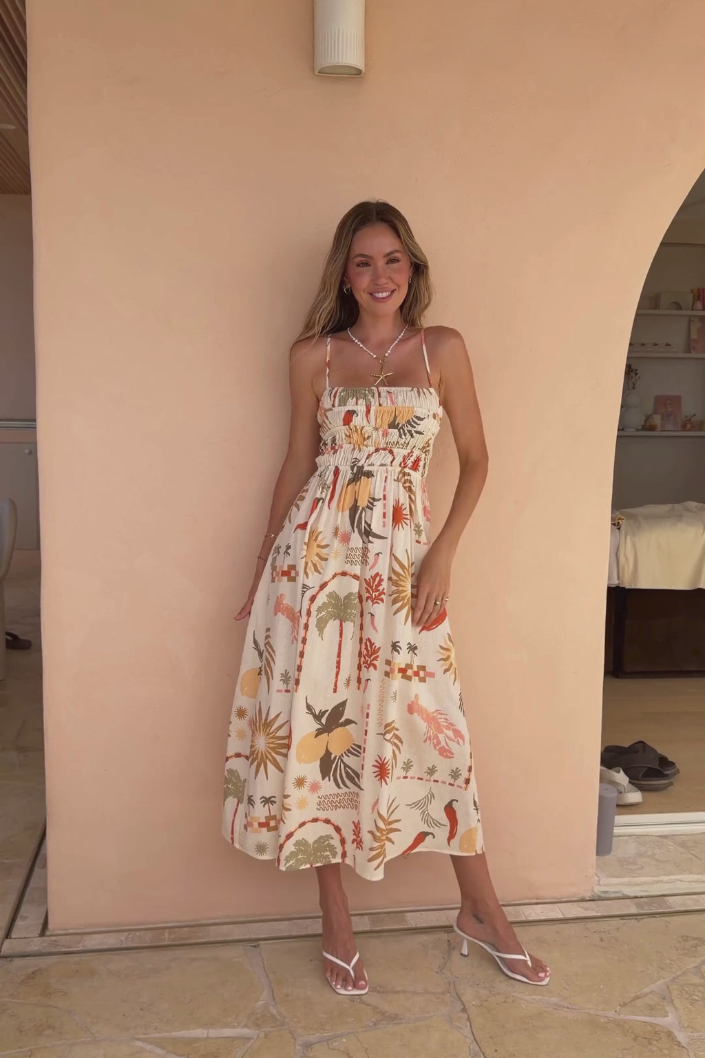 Woman in a floral dress standing by a beige wall