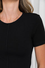Close-up of a woman wearing a black short-sleeve crewneck top, showing the neckline and upper torso against a light neutral background.