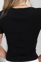 Close-up back view of a woman wearing a fitted black short-sleeve top with a visible center seam and a delicate gold necklace.